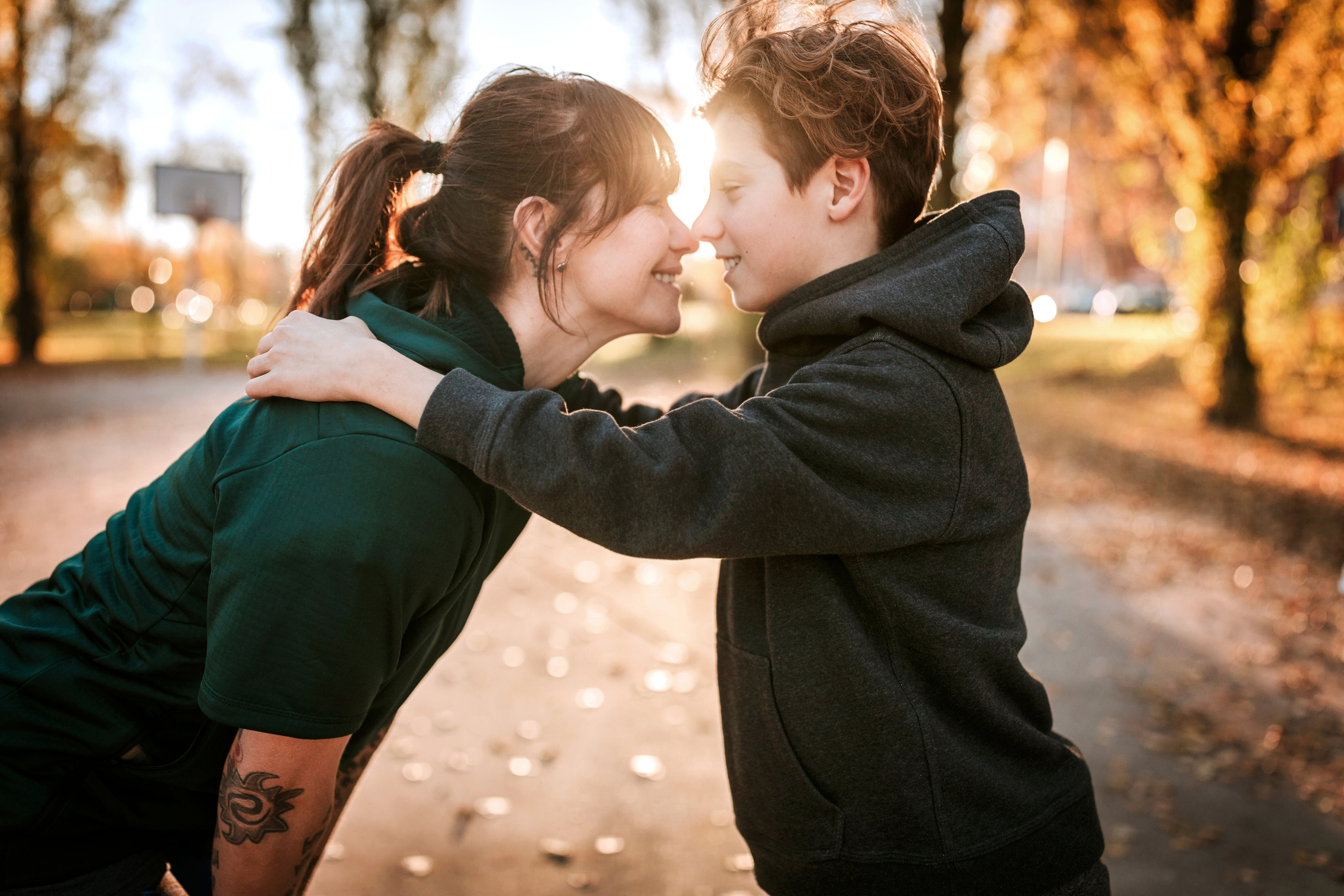 Young woman kissing and embracing her son outdoor, standing face to face on sunny day