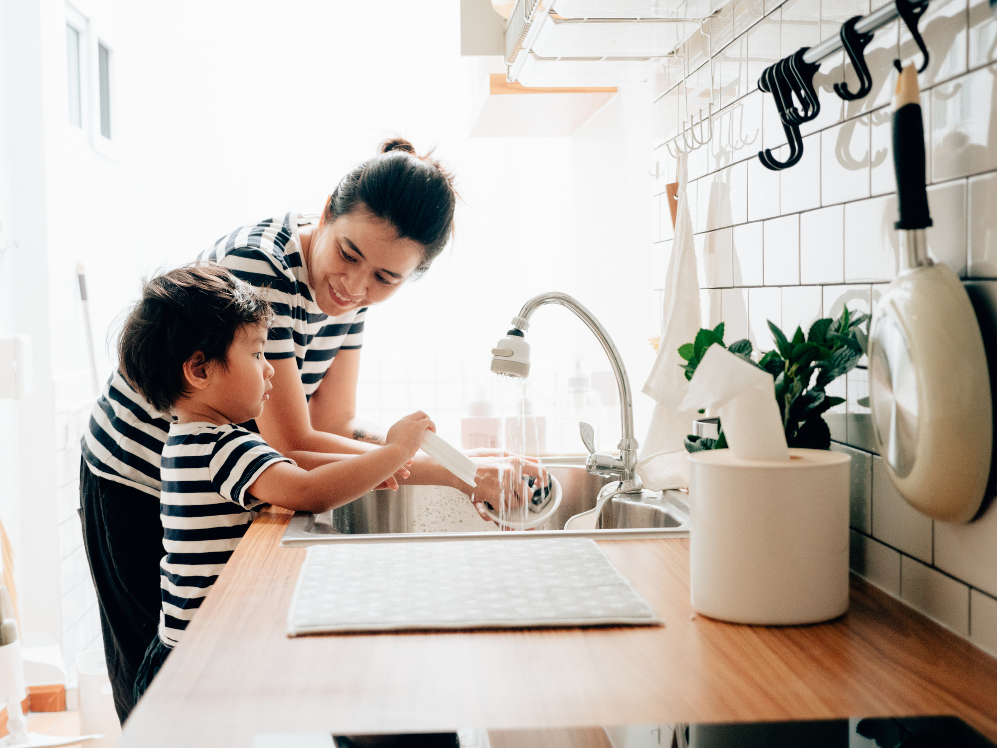 Asian baby boy learn to washing dish with his mother in kitchen.