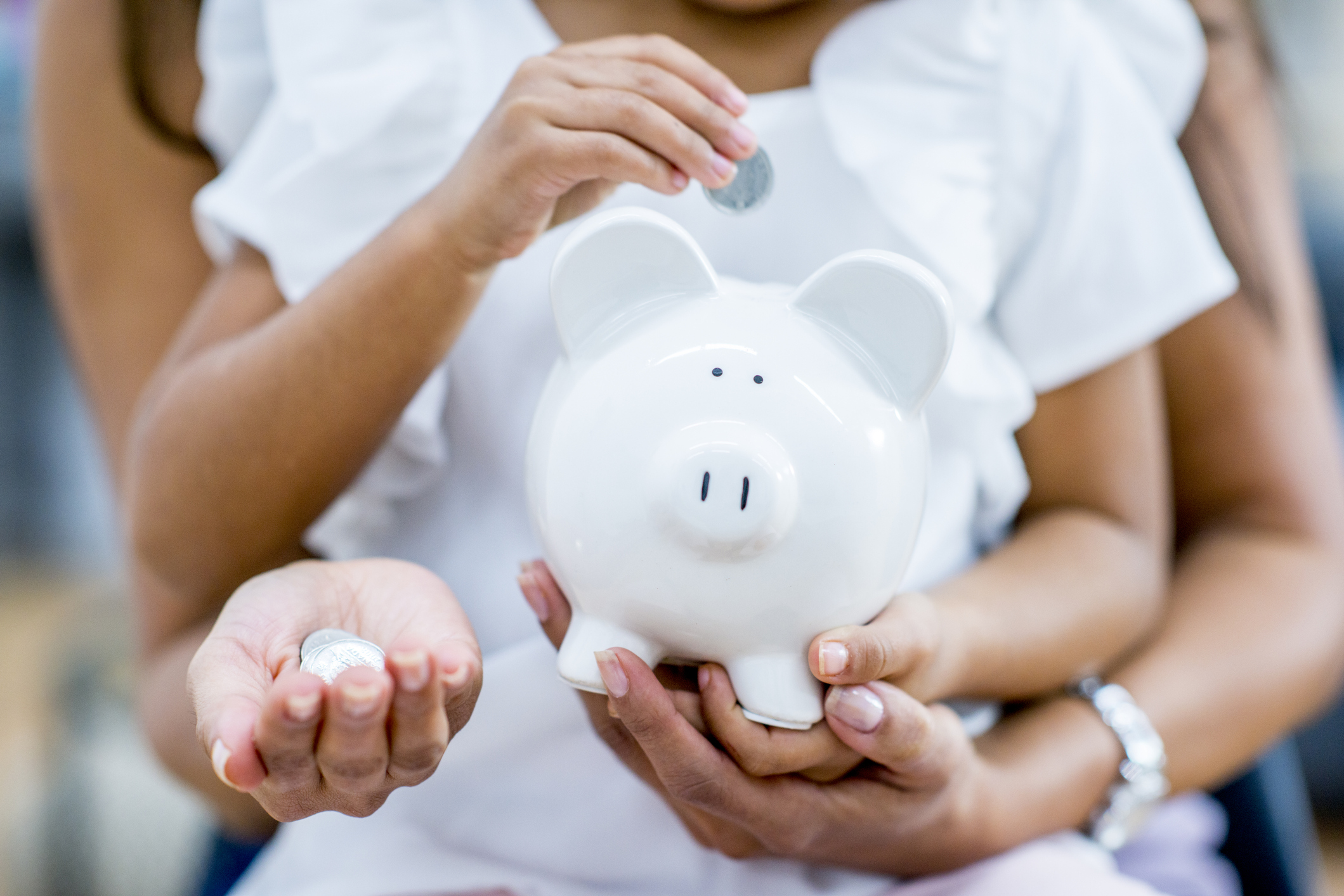 A mother and daughter are holding up a piggy bank. The daughter is putting coins into the bank.