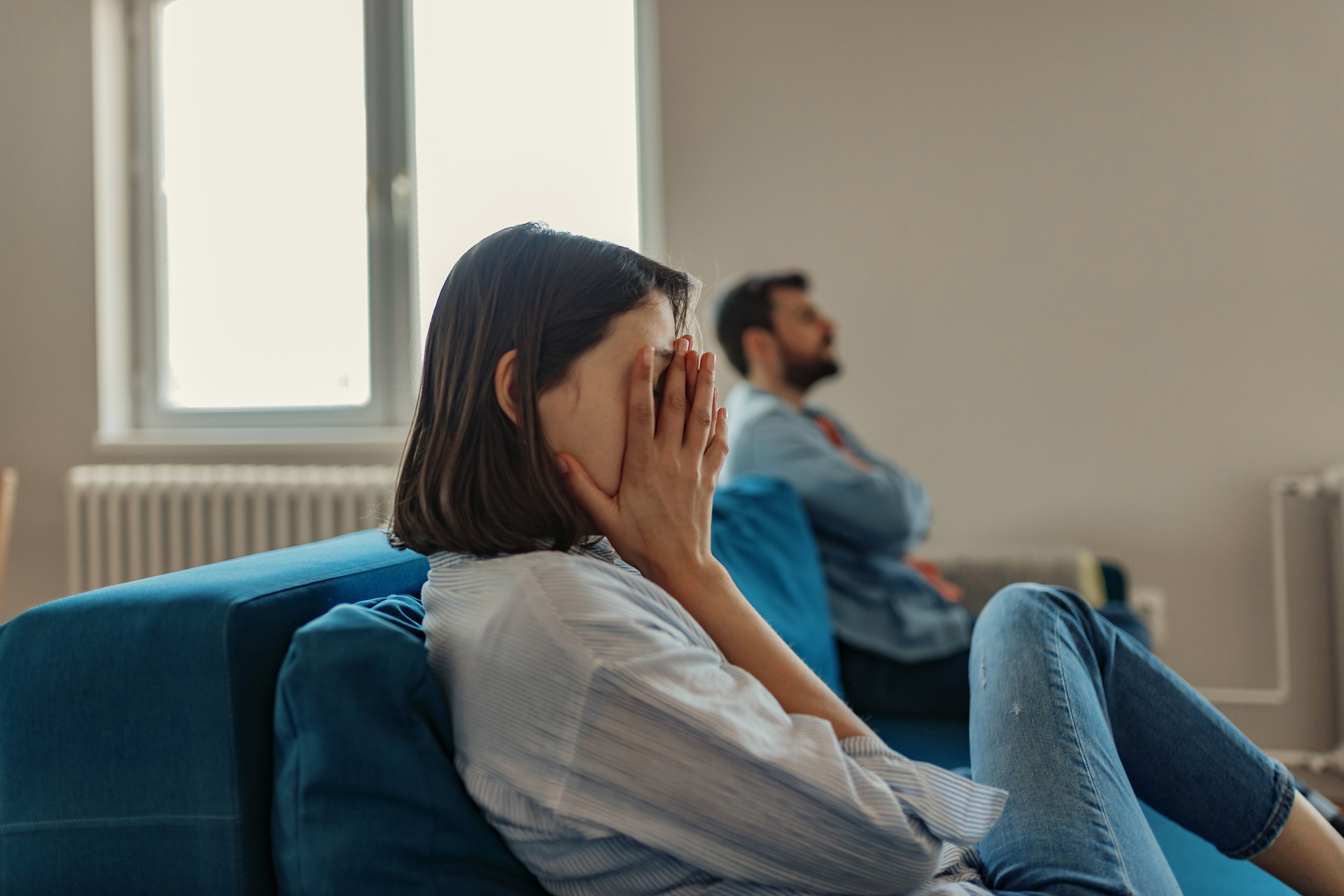 Unhappy Couple After an Argument in the Living Room at Home. Sad Pensive Young Girl Thinking of Relationships Problems Sitting on Sofa With Offended Boyfriend, Conflicts in Marriage, Upset Couple After Fight Dispute, Making Decision of Breaking Up Get Divorced